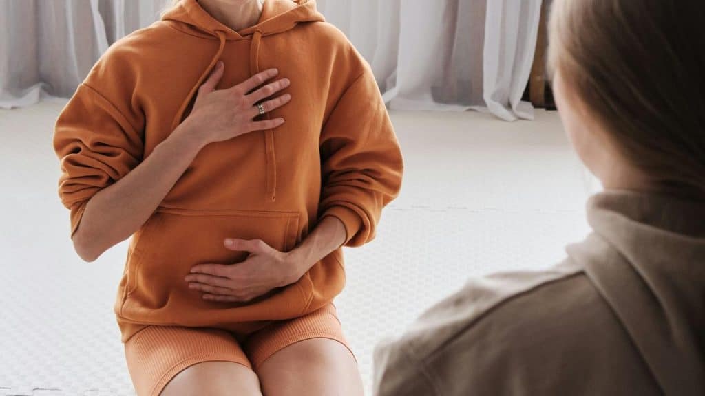 A person seated indoors with hands resting on their chest and stomach.