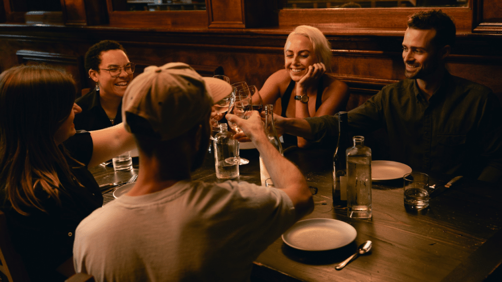 A group of people sit around a table at night, clinking wine glasses in a toast.