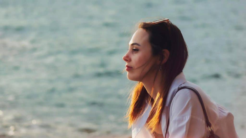 A woman gazes thoughtfully at the sea while sitting near the water.