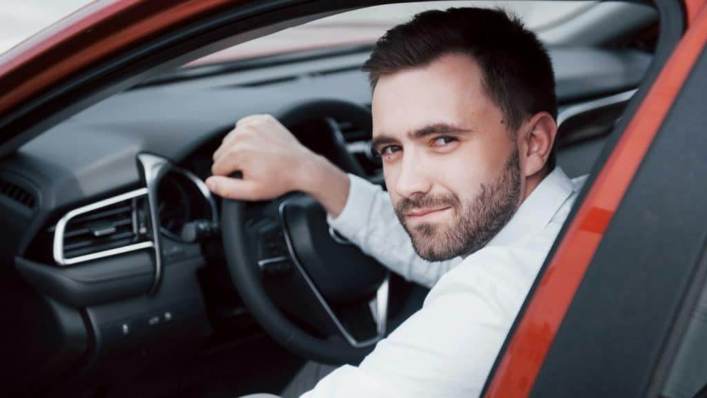 A man in a white shirt sits in the driver's seat of a car looking backward.