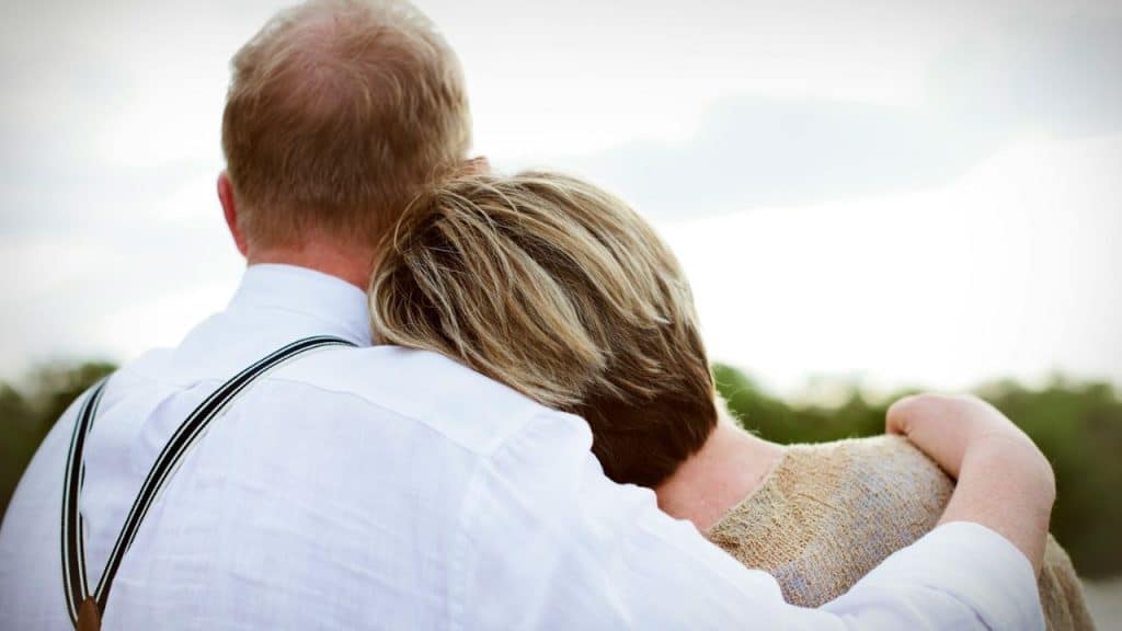A man in a white shirt and suspenders has his arm around a woman's shoulder.