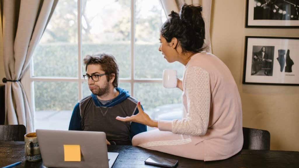 Woman speaking forcefully to a man working on a laptop at a table.