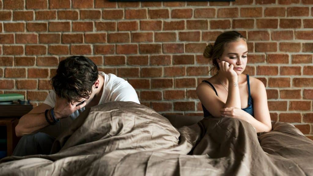 A frustrated couple is sitting in bed, looking away from each other.