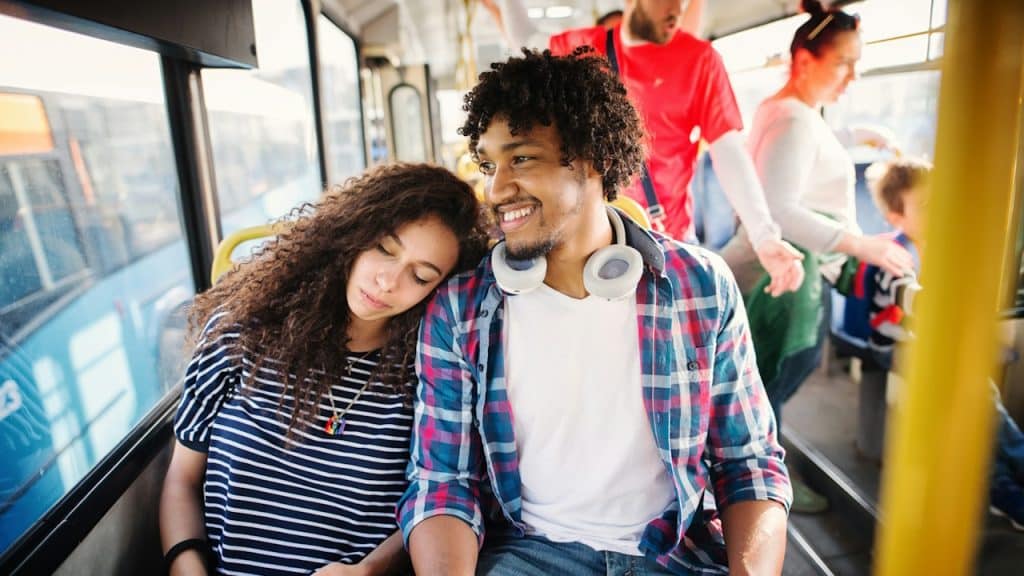 A woman resting her head on a smiling man’s shoulder as they are travelling on a bus.