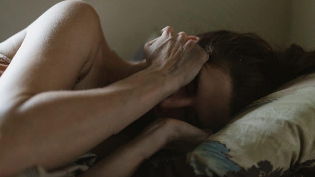 A woman lying in bed with her hands covering her face.