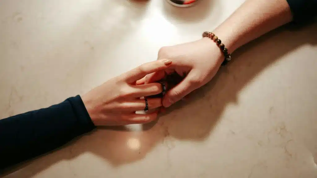 Close-up of a woman’s hand with rings gently touching a man’s hand on a table.