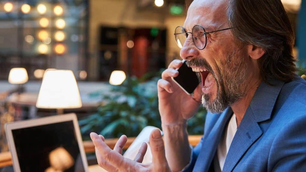 A man angrily shouting into a phone in a warmly lit café.