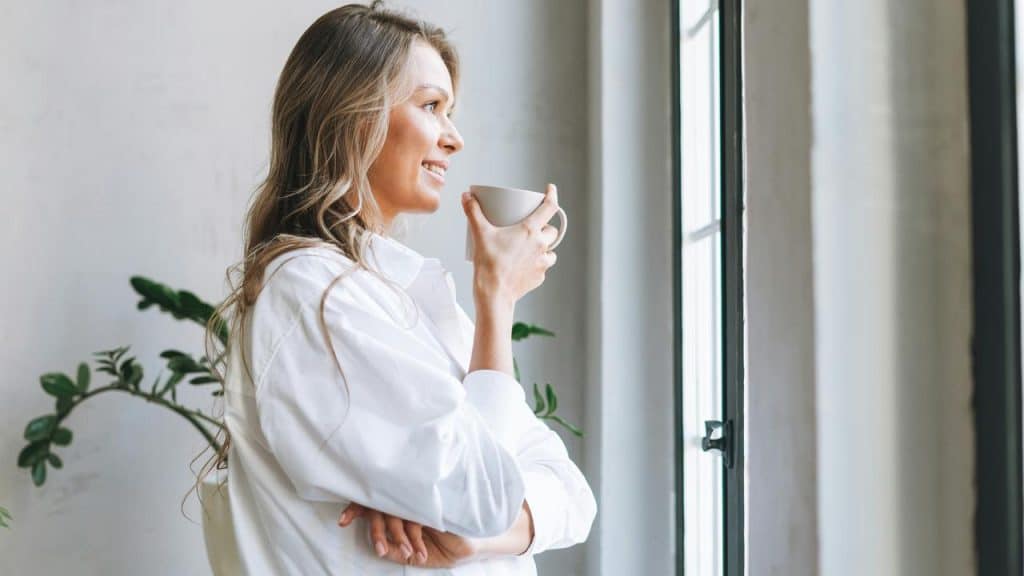 A woman holding a cup and looking out the window.