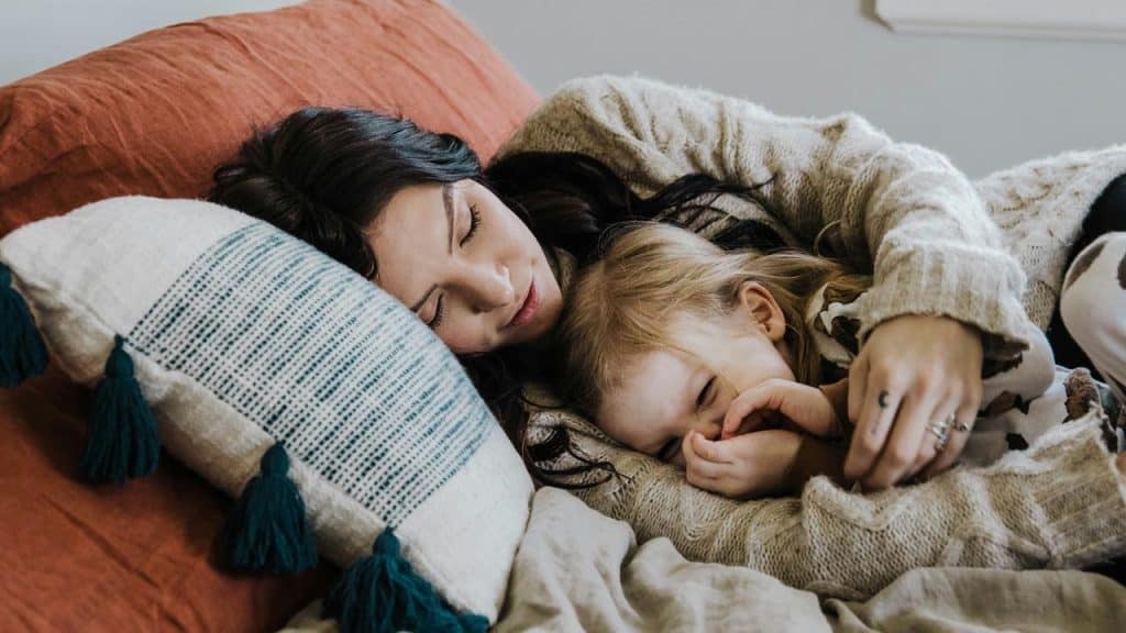 A mother cuddling with her child while laying in bed.