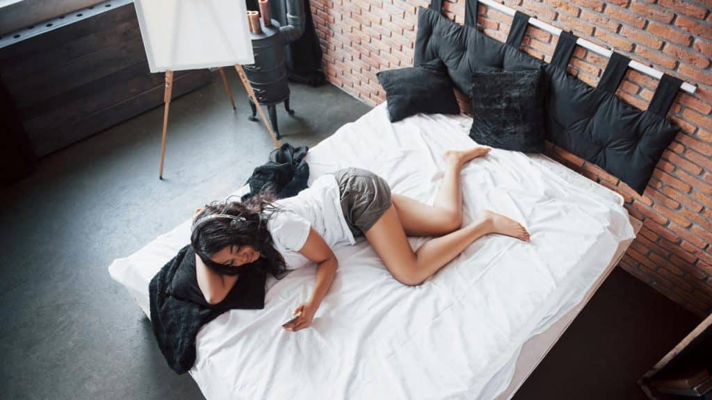 A woman lying on a bed wearing headphones and relaxing.