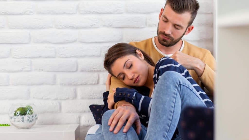 A woman rests her head on a man's shoulder while he holds her gently.