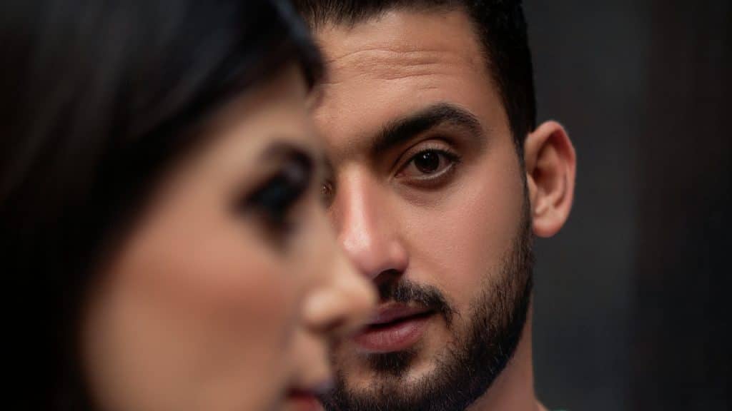 A close-up of a man's face looking forward with a woman's face blurred in the foreground.