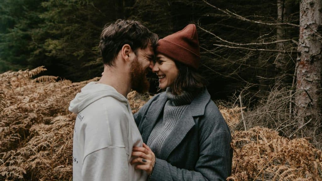 A smiling couple touching foreheads in a forest.