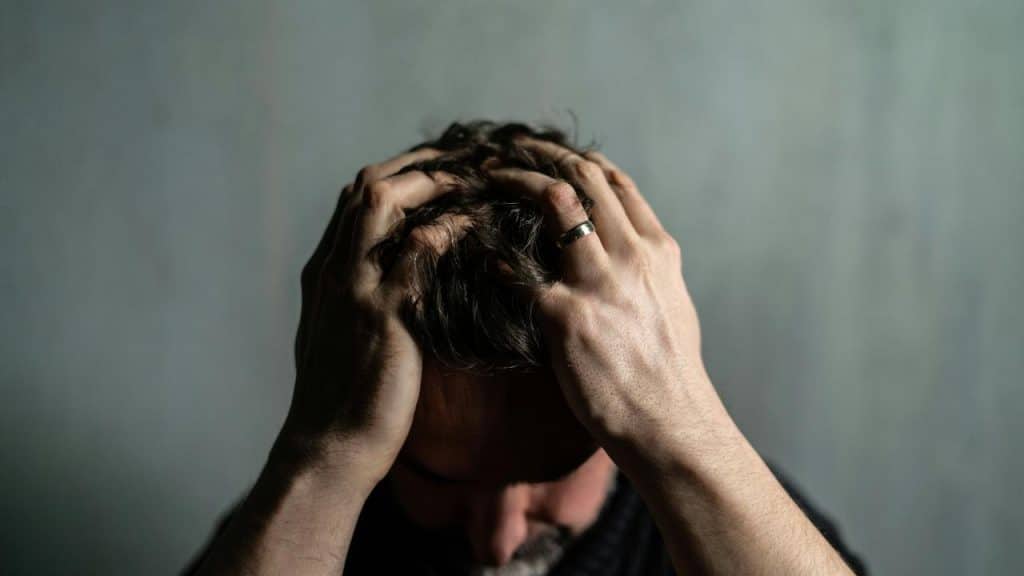 A man holds his head with both hands against a plain background.