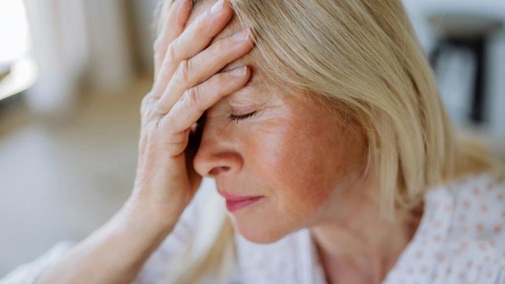 A woman resting her hand on her forehead with eyes closed in a quiet indoor setting.