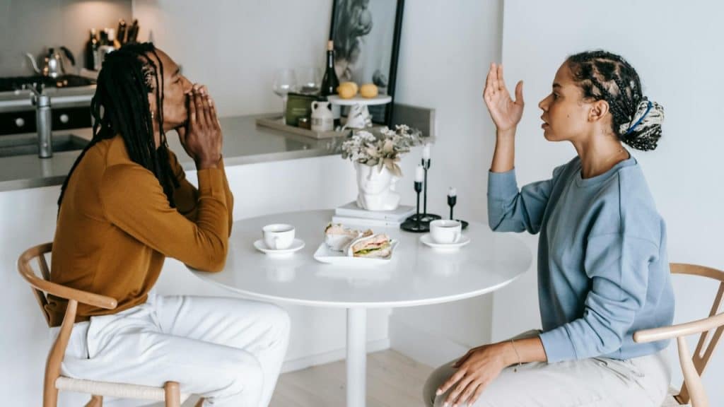 Two people sitting at a white table, one gesturing with a hand while the other listens.