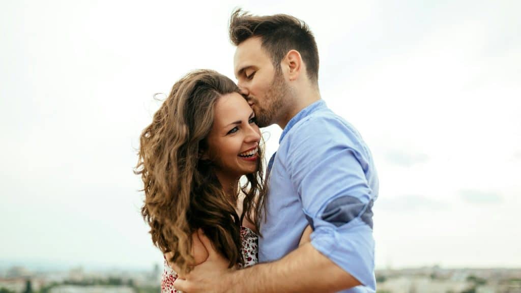 A man kissing a smiling woman’s temple.