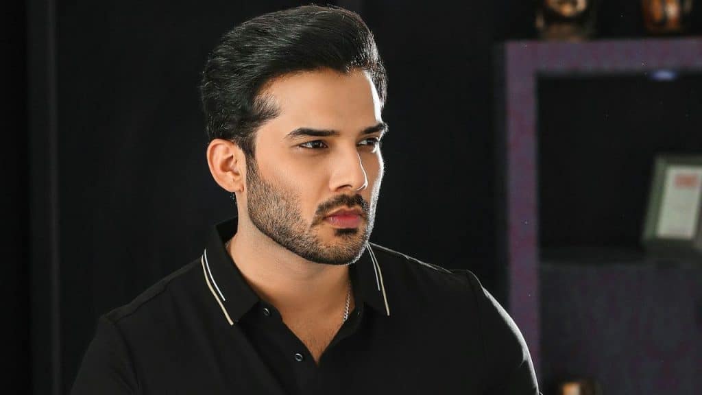A man with a beard and dark hair looks toward his right against a dark background.