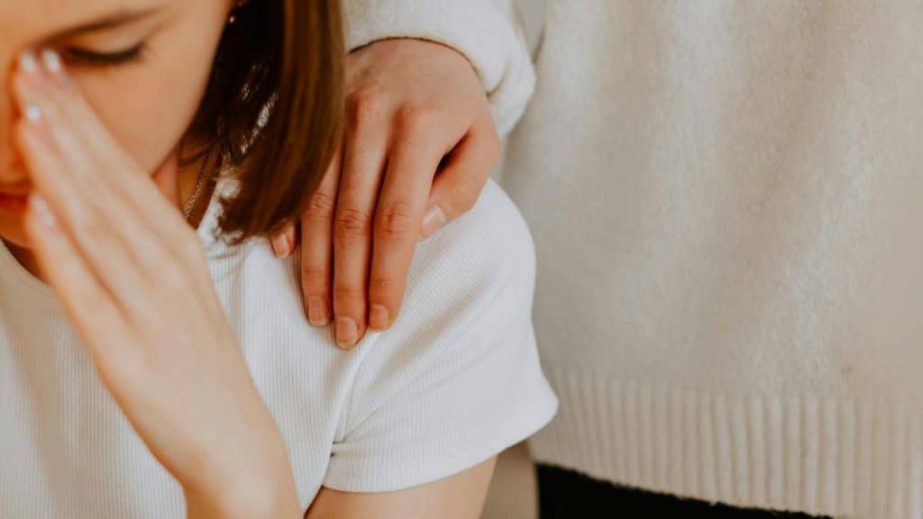 A hand resting gently on a person’s shoulder in a comforting gesture.
