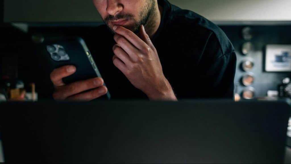 A man using a phone and in front of a laptop