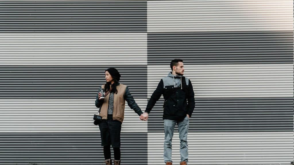 A man and woman looking away while holding each other's hands.