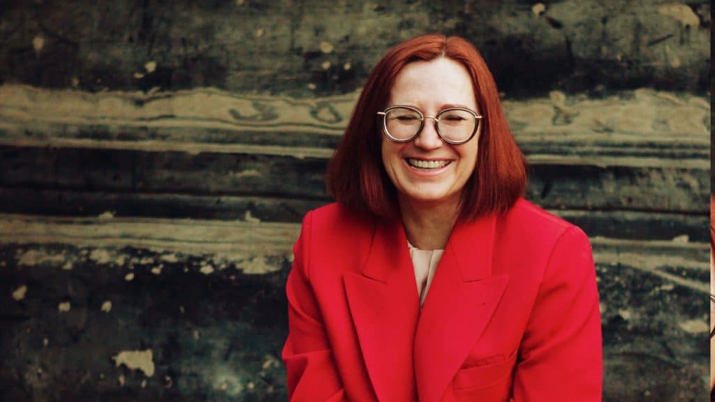 A woman in a red blazer and black skirt sitting on brown concrete stairs.