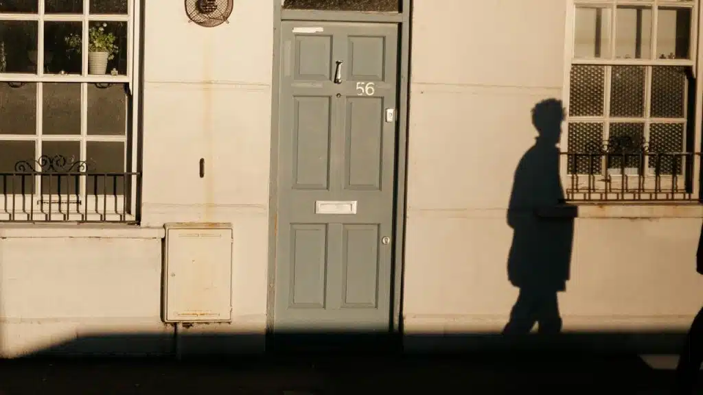 A person's shadow is cast against a light-colored wall next to a blue wooden door.