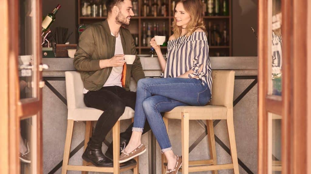 A couple having coffee together at a modern café bar, smiling and chatting on high stools.