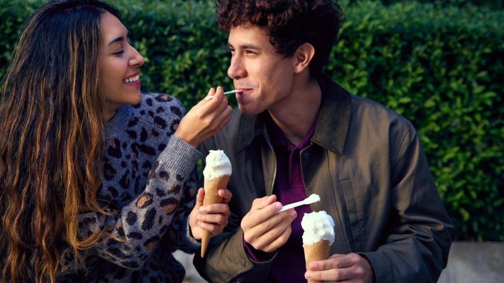 A young couple sharing ice cream and smiling outdoors.