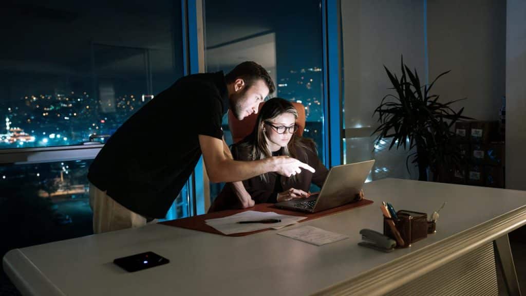A man and woman working late together at a desk with a laptop.