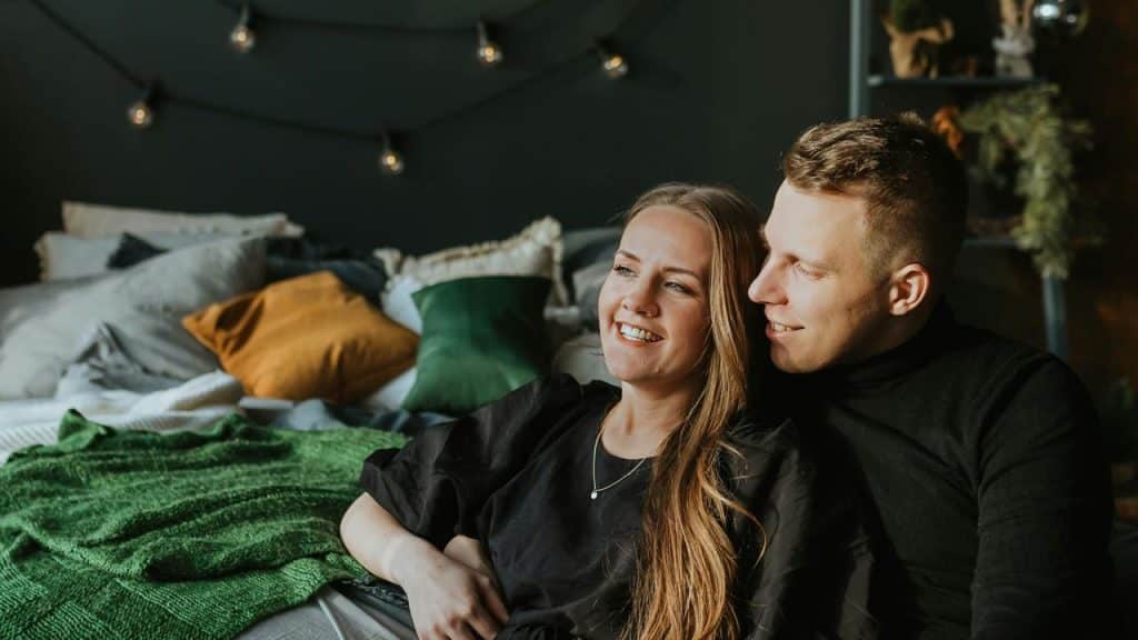 A smiling couple relaxing together on a bed in a cozy bedroom.