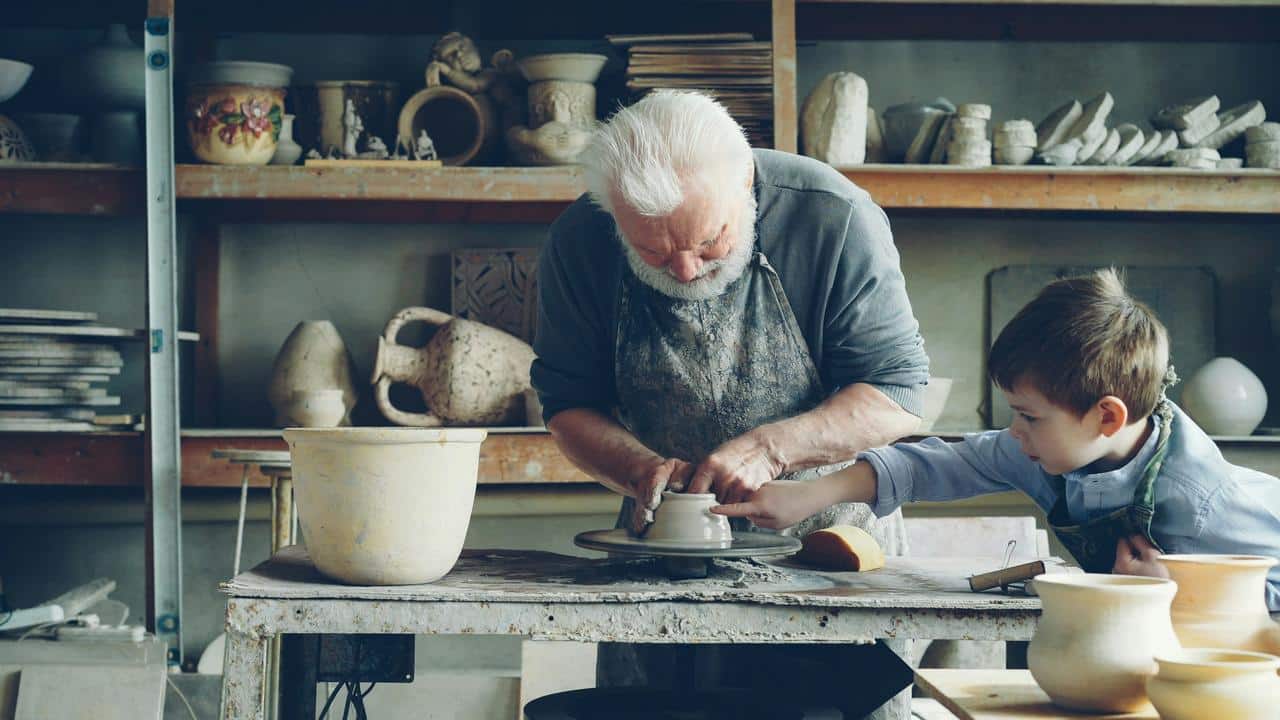 An older man teaching pottery to a young boy.