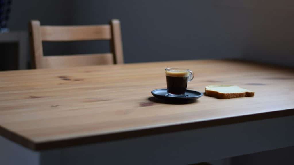 A small cup of espresso and a slice of bread sit on a wooden table.
