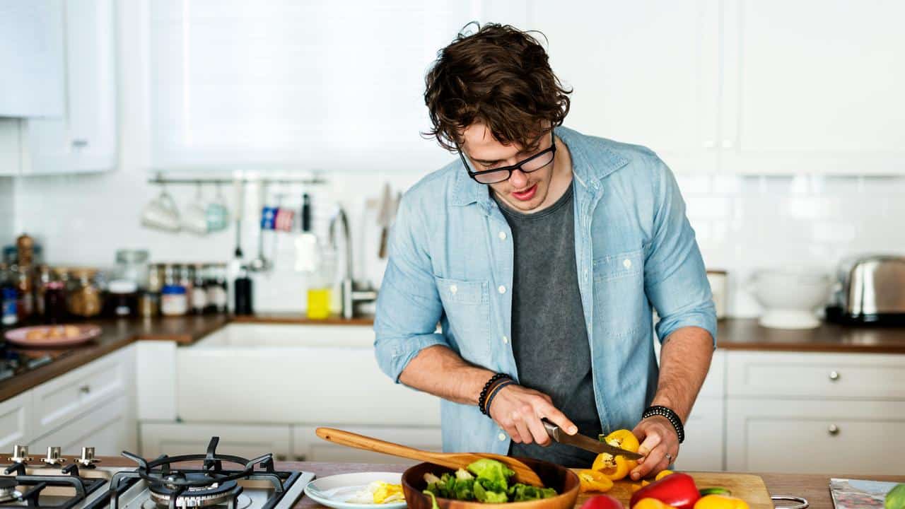 A man slicing a bell pepper over a salad bowl in a kitchen.