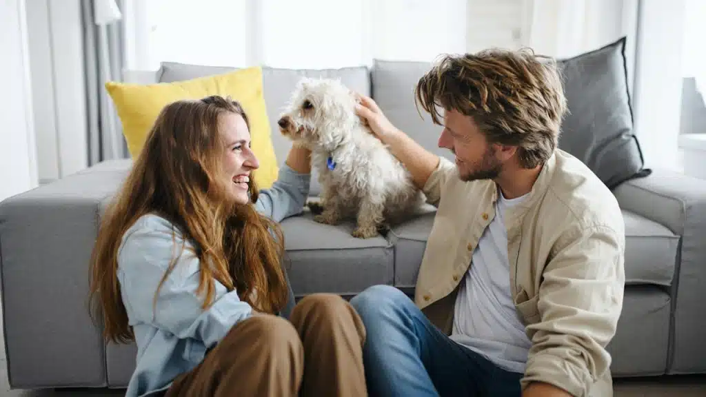 A couple playing with a dog while smiling at each other and talking.