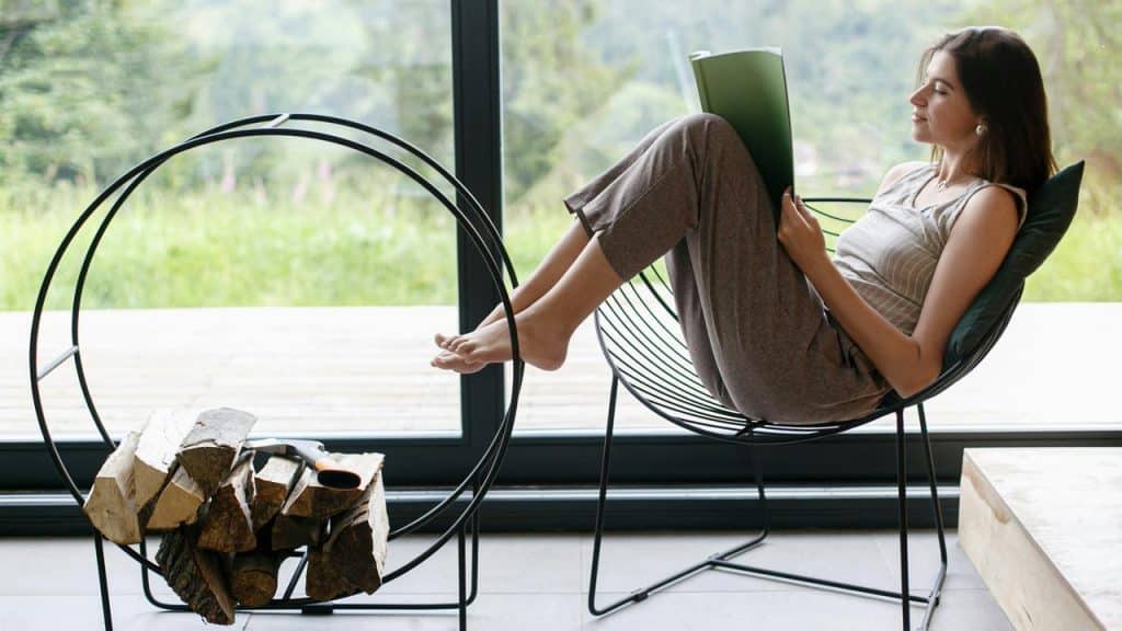 A woman relaxing in a chair while reading near a large window.