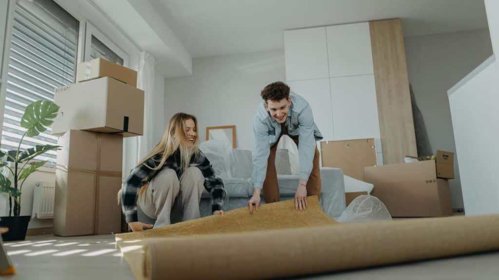 A couple unrolling a rug while unpacking boxes in a new apartment.