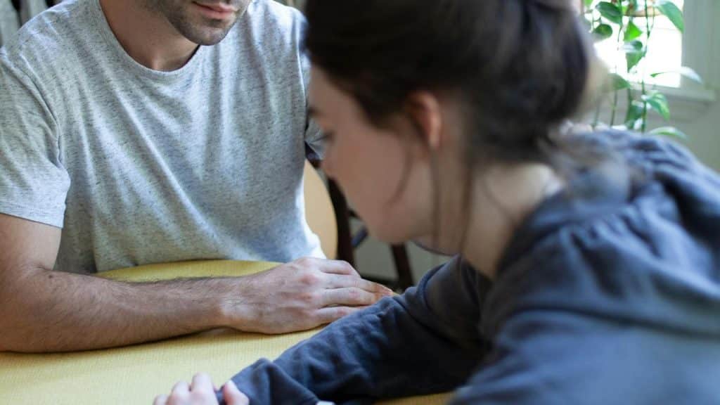 A man and a woman sitting close together at a table indoors, focused on their hands.