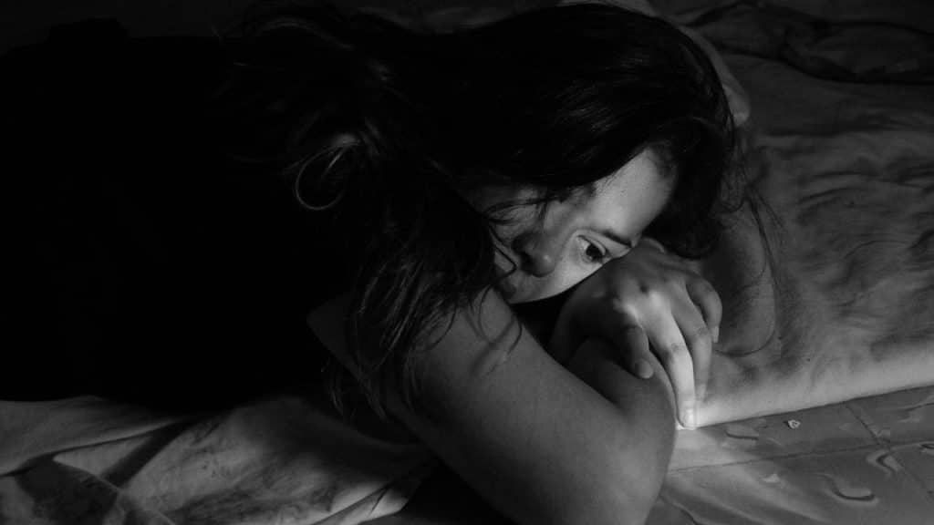 A woman lying on a bed in black and white, resting her head on her arm.