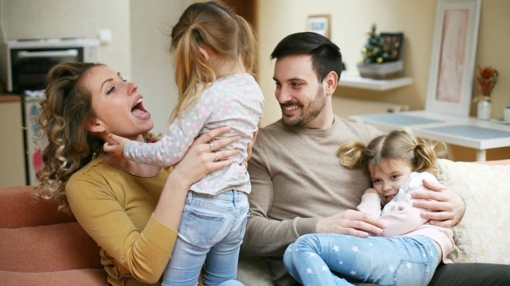 A family with two young children laughing and playing on a couch.