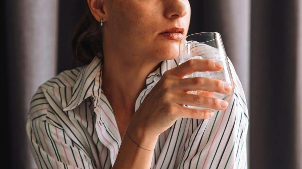 A woman in a striped shirt holding a glass of water with ice.