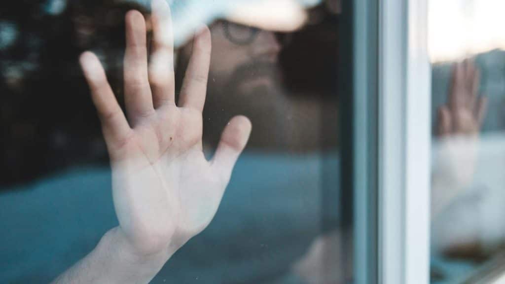 A person pressing their hand against a window with their face blurred in the background.