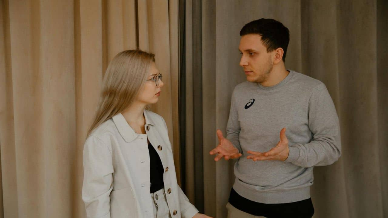 A woman in glasses and a man in a grey sweatshirt having a serious conversation.