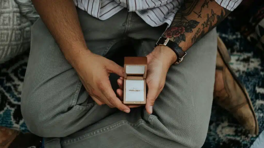 Overhead view of a person with a tattooed arm holding an open ring box with a ring.