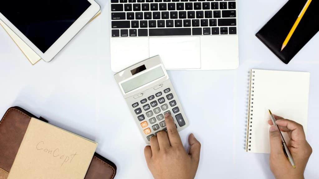 A workspace with a laptop, calculator, tablet, and notebook.