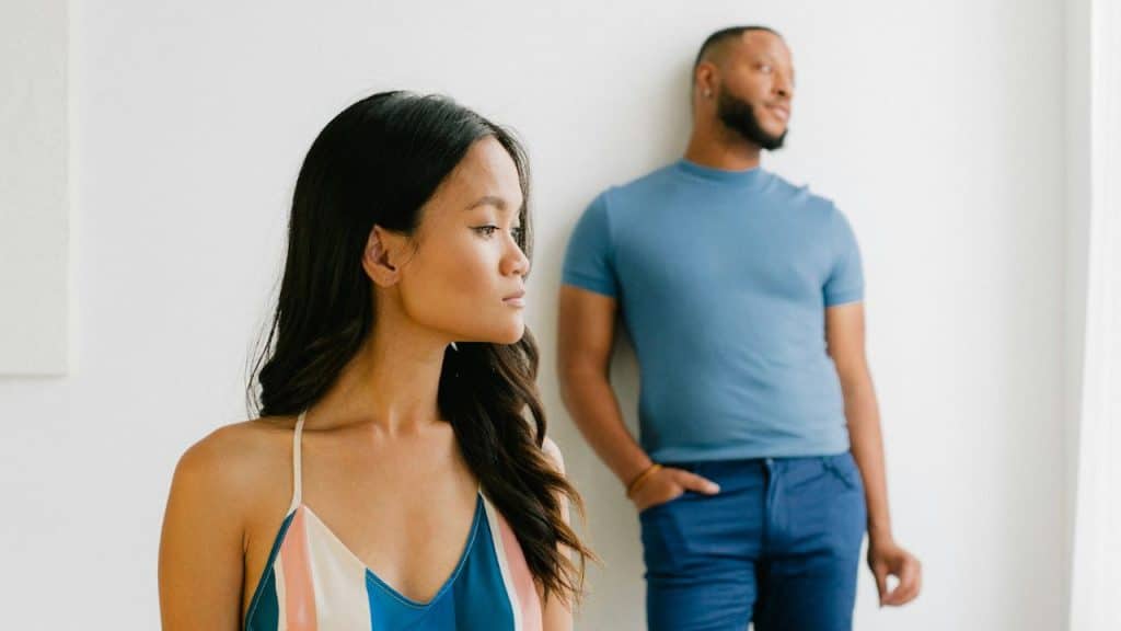 A woman looks toward the side while a man stands blurred in the background.