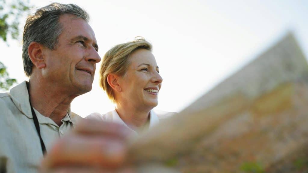 A smiling couple looks into the distance while holding a map outdoors.