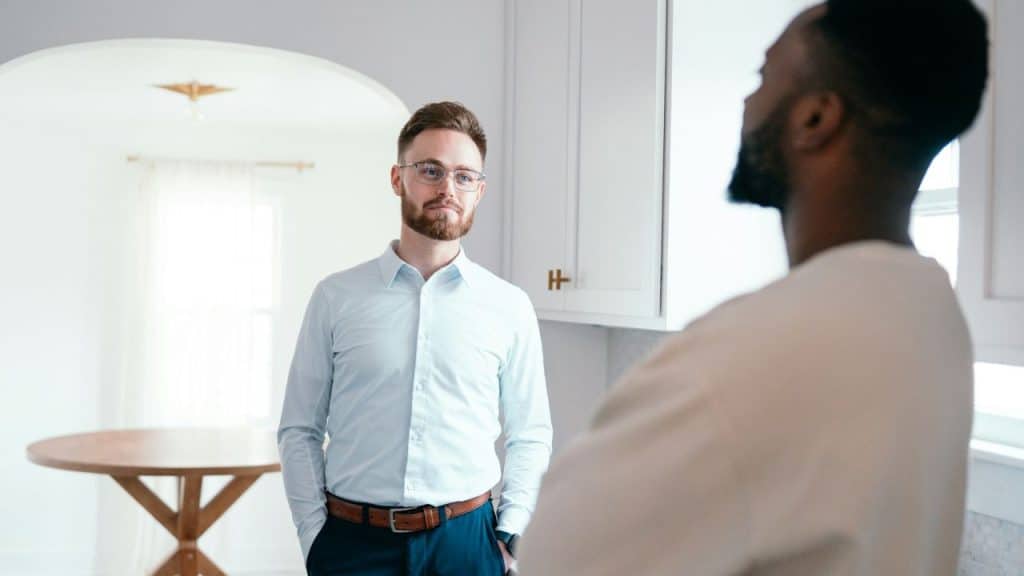 A man in a light blue shirt and glasses looks toward a person in the foreground.