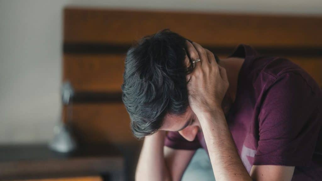 A man in a purple shirt sits with his head lowered into his hands.