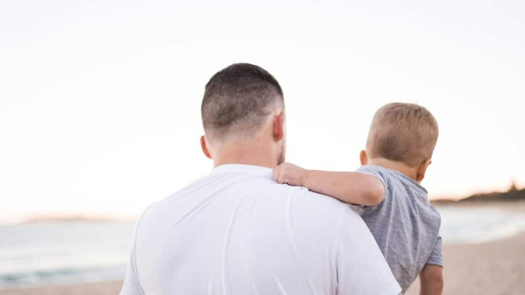 A father carrying his son on his shoulder at the beach.